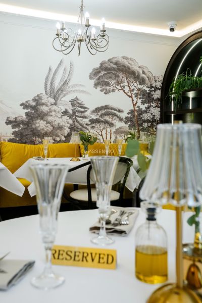 Interior of commercial spaces with white tables, yellow chairs, and a wall mural of a forest.
