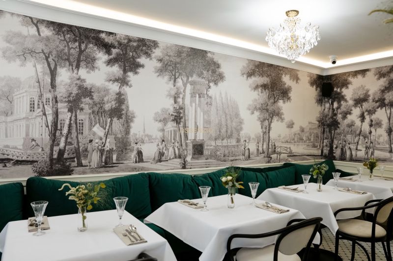 A restaurant with historical wallpaper, a crystal chandelier, and green seating in commercial premises.