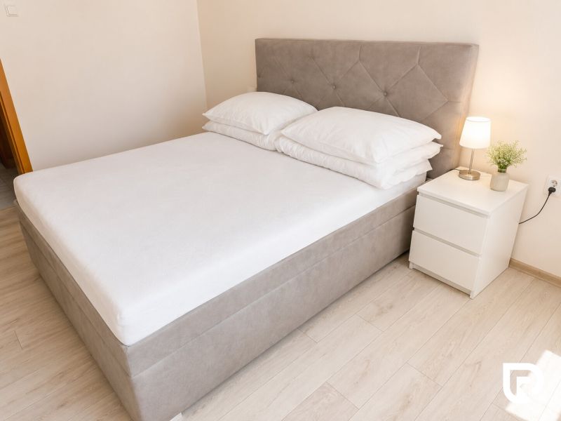 A bed with a nightstand and a lamp in a 2-room apartment on a floor with a wooden decor.