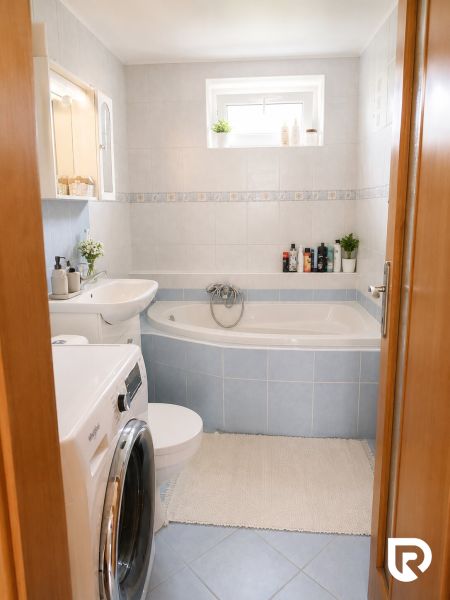 Bathroom in a 2-room apartment with a bathtub, washing machine, and light-colored tiles.