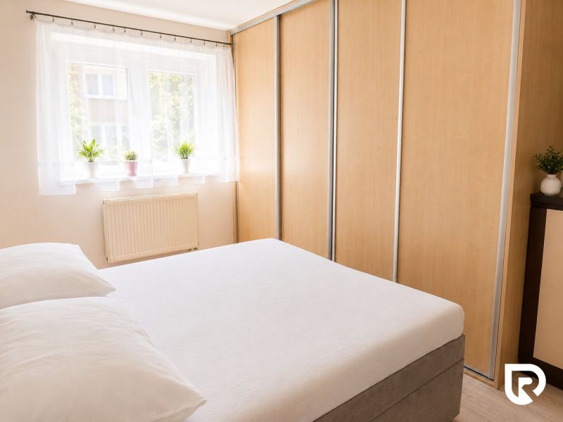 Bedroom in a 2-room apartment with a bed, wardrobes, and a window with plants.