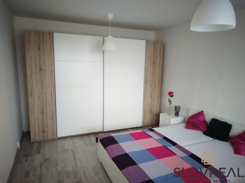 A bedroom with a wooden decor floor in a studio apartment, a wardrobe, and a bed.
