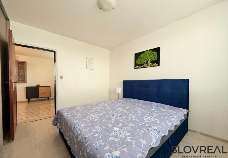 A bedroom with a gray floor in a 3-room apartment, simple furniture, and a painting on the wall.