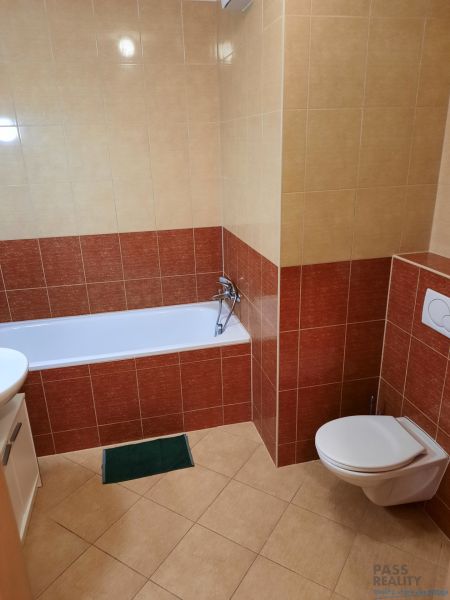 A bathroom with a bathtub and toilet in a 2-room apartment, surrounded by ceramic tiles.