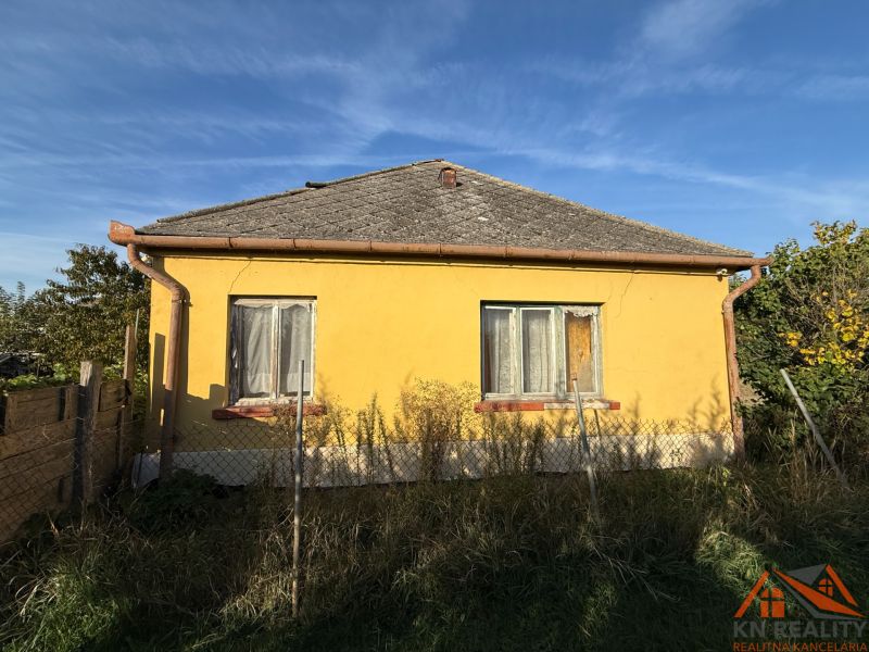 A yellow family house in Komárno with a fence and a garden under the blue sky.