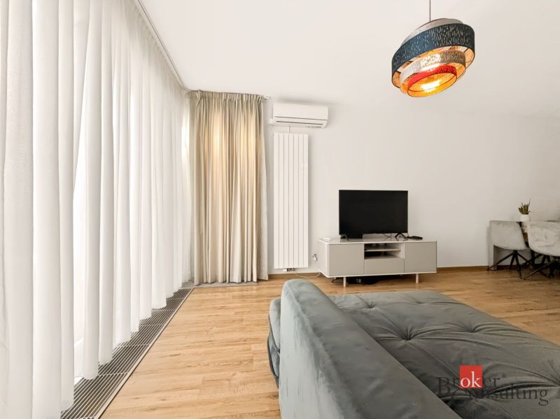 Living room in a two-room apartment with a sofa, TV, and curtains on a floor with wooden decor.