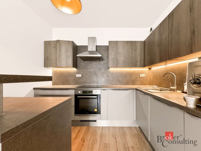 A kitchen in a 2-room apartment with a wooden decor floor and illuminated cabinets.
