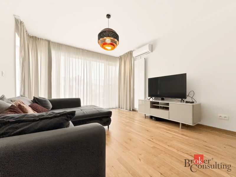 Living room with wood-patterned flooring, a large sofa, and a TV in a 2-room apartment.