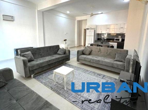 Living room with three gray sofas, a table, and a kitchen in a two-room apartment.