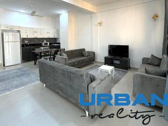 Modern living room in a two-room apartment with a large sofa and a kitchenette.