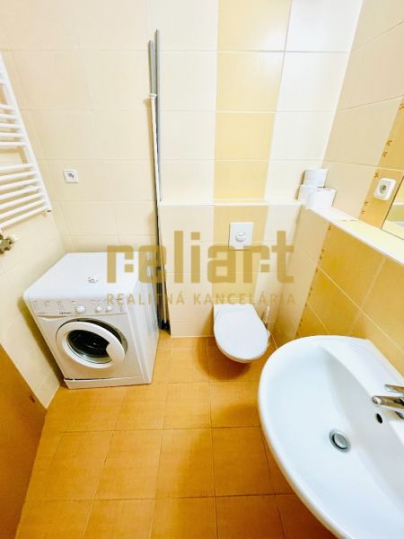 Bathroom in a studio apartment with a washing machine, sink, and toilet.