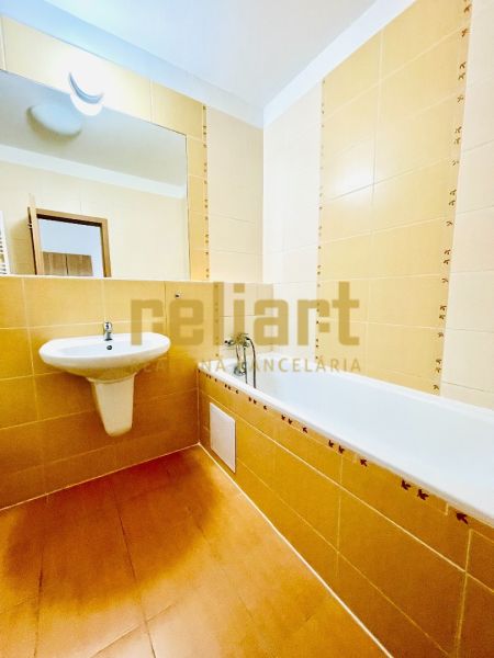 Bathroom in a studio apartment with a bathtub and a sink, light yellow tiles.
