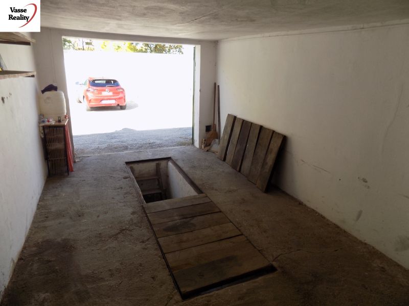 A garage with a service pit, an older concrete surface, and a parked car outside.