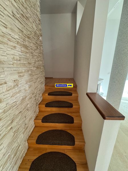 A narrow staircase with brown treads and a wall with a stone decor in a family house.