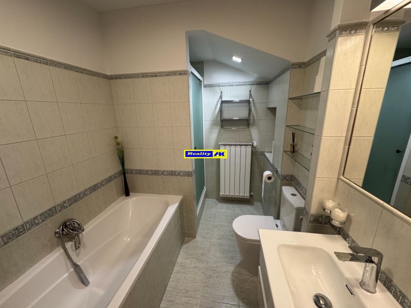 A bathroom in a family house with a bathtub, shower, and light tiles.