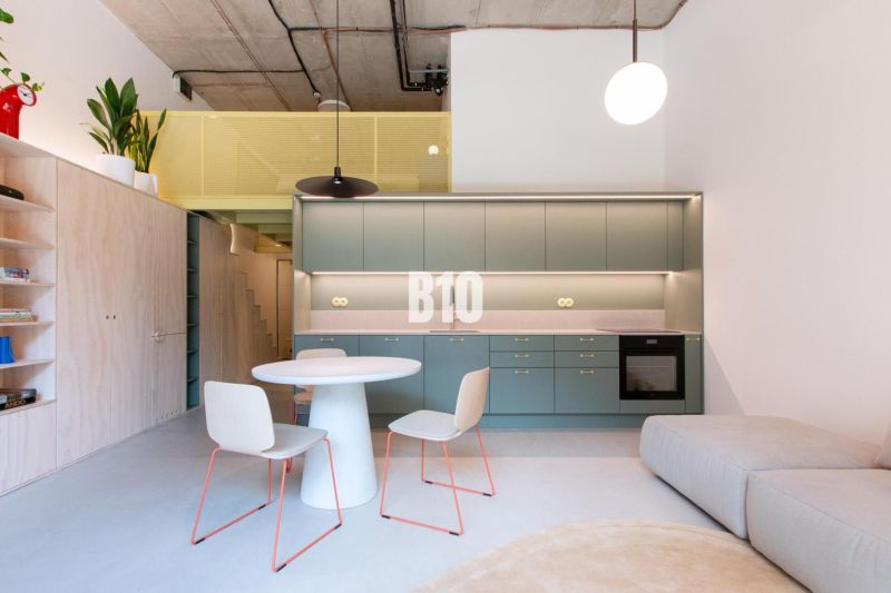 Interior of a 2-room apartment with an open kitchen, seating area, and wooden decor flooring.