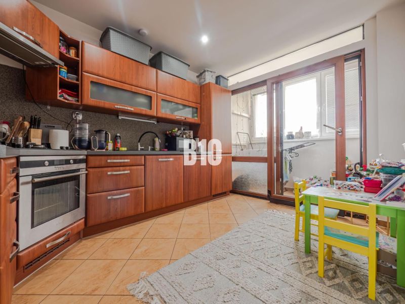 A kitchen in a 3-room apartment with a wooden decor floor and a balcony.