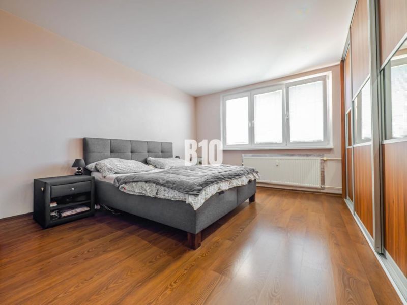A bedroom with a large bed, a nightstand, and a wooden decor floor in a 3-room apartment.