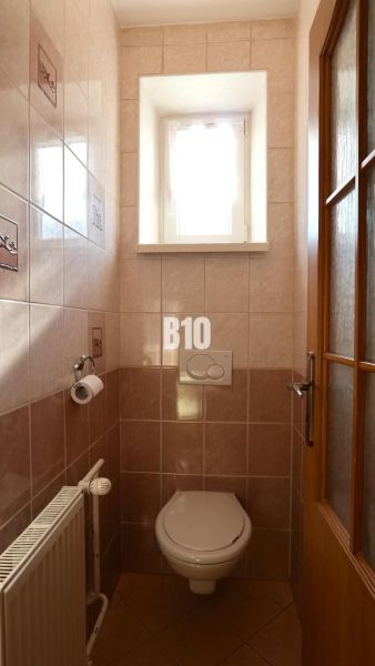 A small bathroom with a window, tiles, and a toilet in a family house.