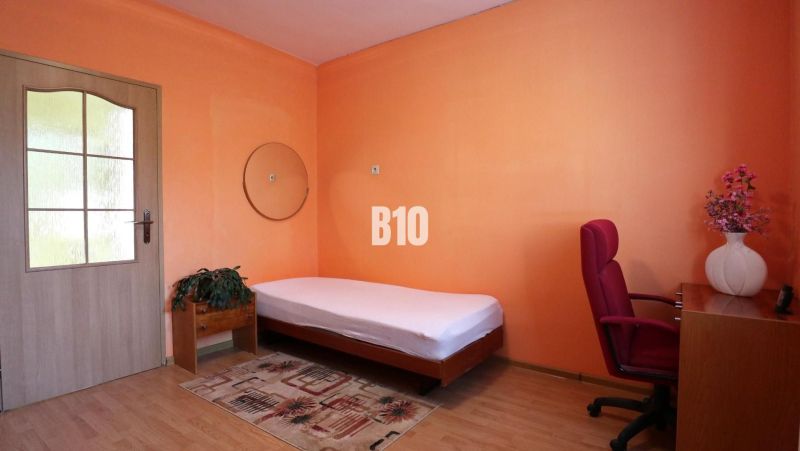 A room in a family house with a bed, a desk, and a wooden-decor floor.