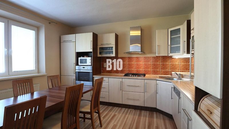 A kitchen with a corner unit, a wooden table, and a floor with a wooden decor.