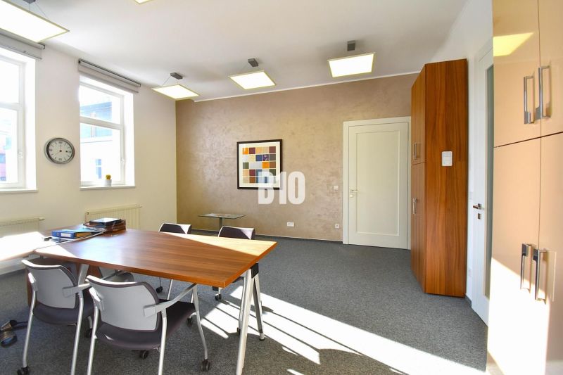 Interior of an office with carpeted floor, desk, chairs, and a wall painting.