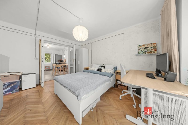 A bedroom with wood-patterned flooring and a desk in a two-room apartment.