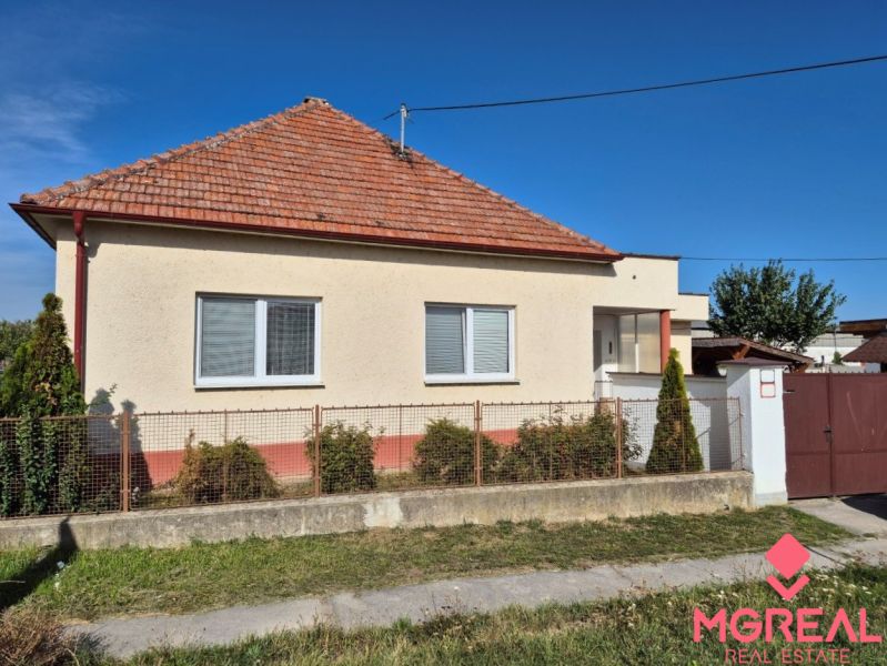 A family house in Ludanice with a white facade and a brick roof, surrounded by a fence.