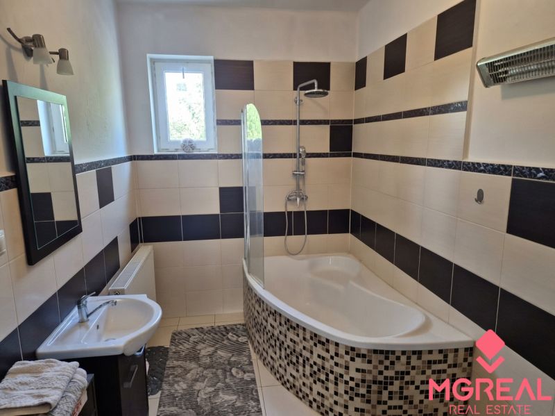 A bathroom in a family house with a bathtub, tiles, and a window; modest furnishings and a light fixture.