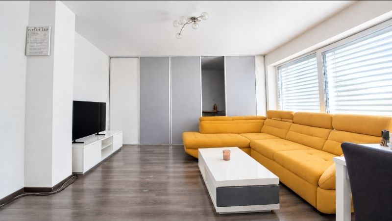 Living room in a family house with a yellow sofa, TV, and a wooden decor floor.