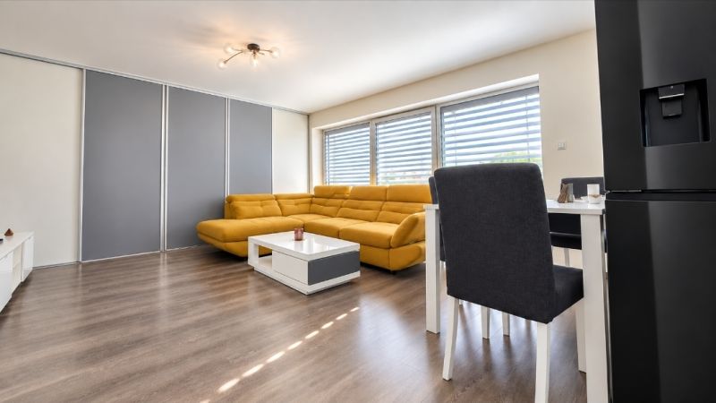 A living room with wood-patterned flooring, a yellow sofa, and a dining table.