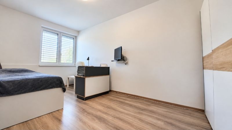A bedroom in a family house with a bed, a table, and a wooden decor floor.