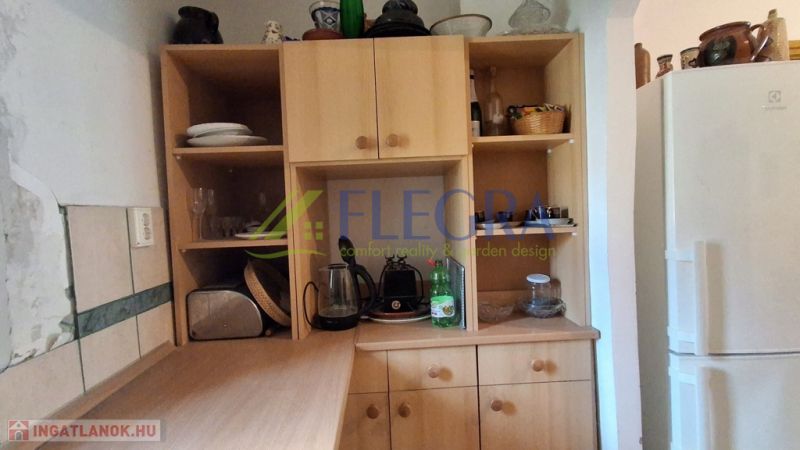 A kitchen cabinet in a family house with shallow shelves and a white refrigerator.