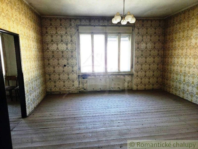 A room with wallpaper and a wooden decor floor, illuminated by a large window.