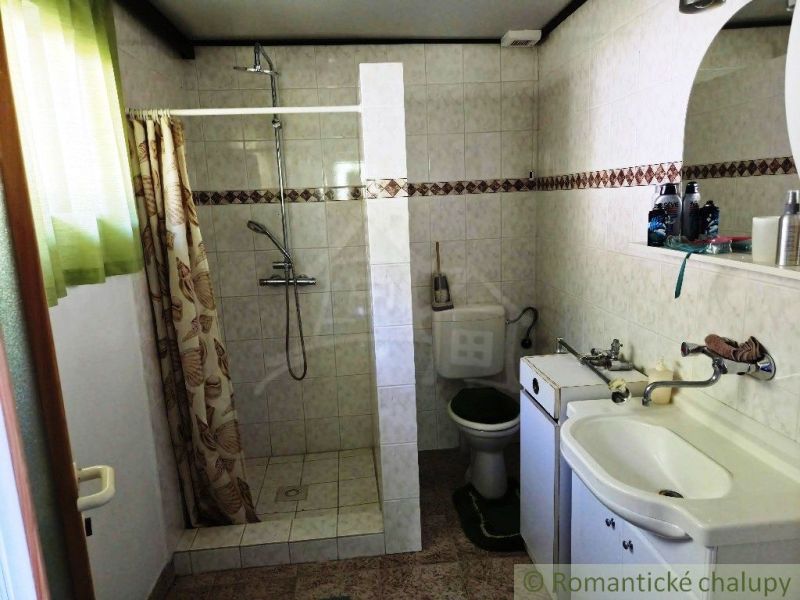 Bathroom in a cottage with white tiles, a shower, and a sink with a mirror.