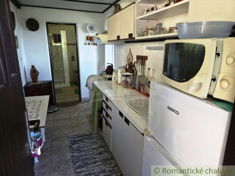 A kitchenette in a cottage with white cabinets and appliances, next to a bathroom.