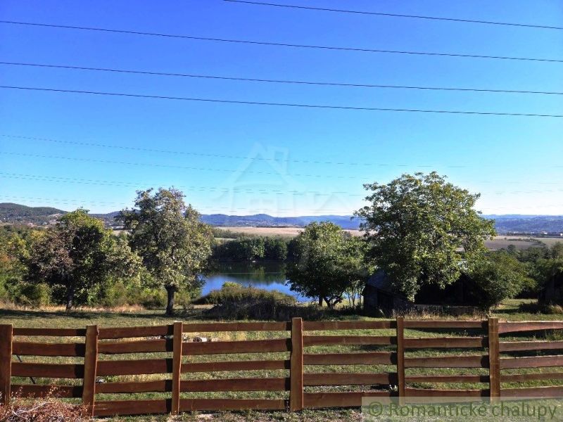 View of the lake from the garden in Krupina, surrounded by greenery and a wooden fence.
