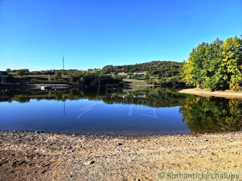 A peaceful body of water in the Gardens in Krupina surrounded by greenery and a blue sky.