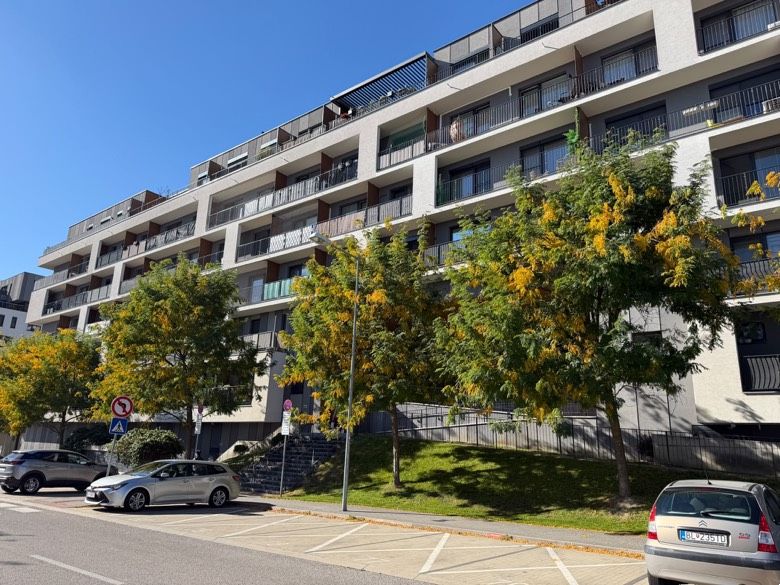Apartment building in Bratislava-Petržalka with greenery and parking spaces in front of the entrance.