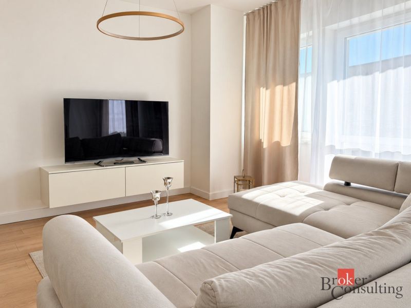 A bright living room with a sofa, television, and wood-decor flooring in a studio apartment.