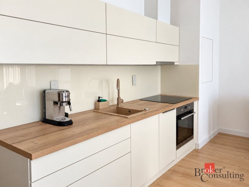 Kitchen in a studio apartment with wood decor flooring, cream cabinets, coffee maker.