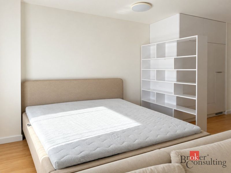 Bedroom in a studio apartment with a bed and white shelves, floor with wood decor.