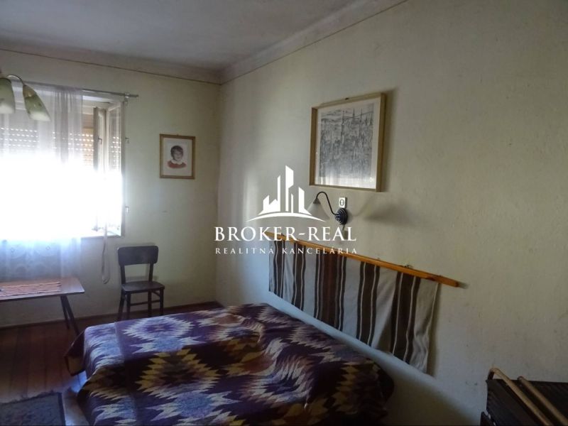 A room in a family house with a chair, a bed, and a wooden-patterned floor.